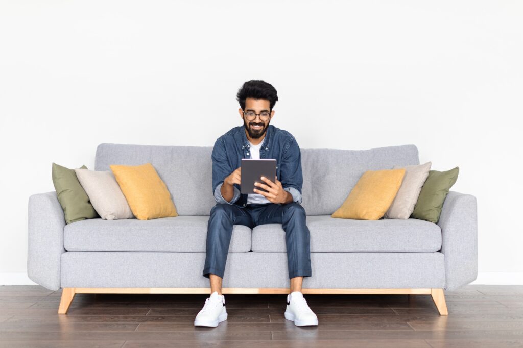 Relaxed Indian Guy Browsing Digital Tablet While Sitting